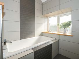 A bathroom with a bathtub, tiled walls, a window with a wooden sill, and a vase with green foliage at Criw in Bryncroes near Sarn Meyllteyrn