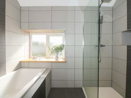 A bathroom with a bathtub and a glass-enclosed shower area with a window shelf holding a vase of greenery at Criw Bryncroes near Sarn Meyllteyrn