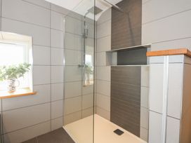 A tiled shower area with a glass door and a small window with a vase of leaves at Criw Bryncroes near Sarn Meyllteyrn