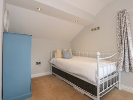 A bedroom with a single white metal bed with pillows a blue dresser a wall clock patterned curtains and beige carpet at Criw Bryncroes near Sarn Meyllteyrn
