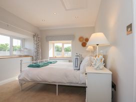 A bedroom with a white bed and green towels on it beside two windows with curtains and blinds at Criw in Bryncroes near Sarn Meyllteyrn
