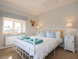 A bedroom with a white metal bed frame two bedside tables with lamps and decorative items and a window with a valance at Criw in Bryncroes near Sarn Meyllteyrn