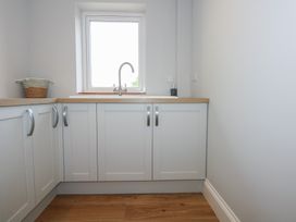 A kitchen corner with white cabinets a window above a sink and a basket on the wooden countertop at Criw in Bryncroes near Sarn Meyllteyrn