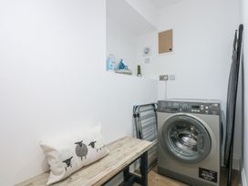 A laundry room with a washing machine bench with a pillow and ironing board at Criw in Bryncroes near Sarn Meyllteyrn