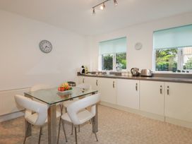 A kitchen with a glass dining table and four white chairs next to cream cabinets and windows with blue blinds at 13 Clock Tower Court in Charlestown