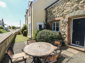 An outdoor patio area with a round stone table and four metal chairs next to a stone and brick house at 5 Cart-Tws Bach in St Davids