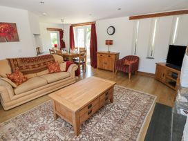 A living room with a beige sofa a wooden coffee table a dining table with chairs red curtains and a television at 5 Cart-Tws Bach in St Davids