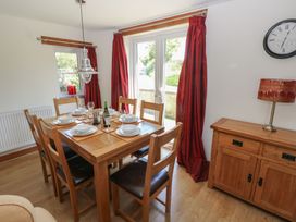 A dining room with a wooden table set for six and red curtains at 5 Cart-Tws Bach in St Davids