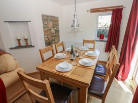 A dining room with a wooden table set for six near a window with red curtains at 5 Cart-Tws Bach in St Davids