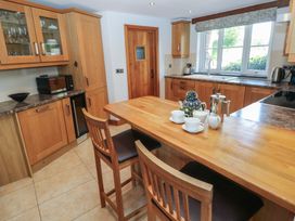 A kitchen with wooden cabinets and a countertop with two wooden chairs and a tea set on the island at 5 Cart-Tws Bach in St Davids