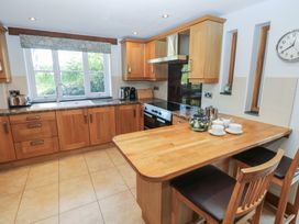 A kitchen with wooden cabinets a countertop with a sink a wooden breakfast bar with two chairs and a clock on the wall at 5 Cart-Tws Bach in St Davids