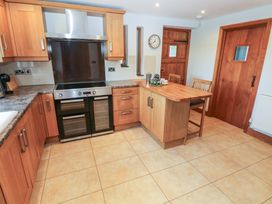 A kitchen with wooden cabinets an oven a kitchen island with stools and tiled floor at 5 Cart-Tws Bach in St Davids