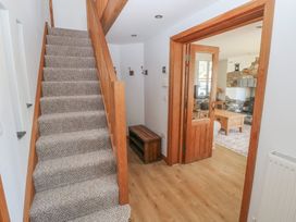 A staircase with carpet next to a hallway leading to a living room with wooden furniture and a stone fireplace at 5 Cart-Tws Bach in St Davids