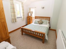 A bedroom with a wooden bed, two windows with curtains, a wooden chest of drawers with a lamp and mirror 5 Cart-Tws Bach St Davids