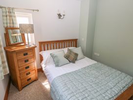 A bedroom with a wooden bed and chest of drawers with a lamp by a window at 5 Cart-Tws Bach in St Davids