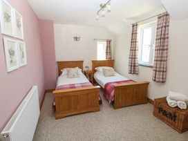 A bedroom with two single wooden beds a window with curtains a radiator and a wicker basket at 5 Cart-Tws Bach in St Davids