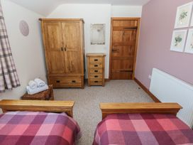 A bedroom with two single beds with checkered blankets wooden wardrobe chest of drawers door and framed pictures on the wall at 5 Cart-Tws Bach in St Davids
