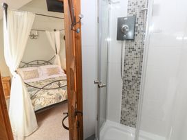 A bedroom with a canopy bed and a shower cubicle separated by a wooden door at 5 Cart-Tws Bach in St Davids