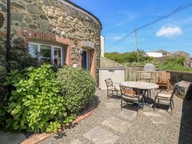 An outdoor patio area with a round table and chairs next to a stone house with plants and a fence at 5 Cart-Tws Bach in St Davids