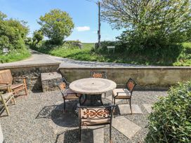 An outdoor patio with a round stone table and four metal chairs with cushions and a gravel ground at 5 Cart-Tws Bach in St Davids