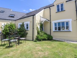A garden with a metal table and four chairs next to a yellow house with white window frames at 5 Cart-Tws Bach in St Davids