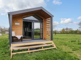 A small wooden cabin with glass sliding doors and a chair on the porch in a grassy field at Elmside Lodge in Welland Malvern