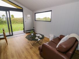 A sitting area with a brown leather sofa and a glass coffee table next to a sliding glass door and window at Elmside Lodge in Welland Malvern