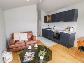 A living area with a brown leather sofa and a glass coffee table in front of a kitchen with dark cabinets and wooden flooring at Elmside Lodge in Welland Malvern