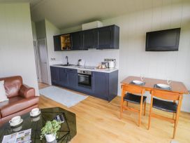 A kitchen area with dark cabinets a small dining table with two chairs a wall-mounted TV and a brown leather sofa at Elmside Lodge in Welland Malvern