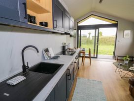 A kitchen area with sink stove and cabinets next to a dining table set near sliding glass doors at Elmside Lodge in Welland Malvern