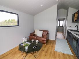 A small living area with a brown leather sofa a black coffee table with cups and a plant a kitchen area with dark cabinets and a blue rug on wooden floor at Elmside Lodge in Welland Malvern