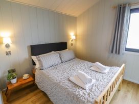 A bedroom with a double bed covered with two folded white towels bedside table with plant and cup wall lamps and window with gray curtains at Elmside Lodge in Welland Malvern