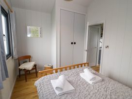 A bedroom with a wooden bed and towels on the bed a wooden chair with a blanket a closet and a door at Elmside Lodge in Welland Malvern