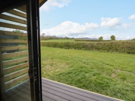 A view of a grassy field and hedge from a wooden deck with a glass door open at Elmside Lodge in Welland Malvern