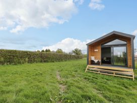 A small wooden cabin with glass sliding doors and a chair on a grass field at Elmside Lodge in Welland Malvern