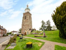 A stone clock tower next to a green park with flowers trees and a statue near a road with houses at Elmside Lodge in Welland Malvern