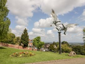 A metal sculpture of two birds on a tall post in a park with flowers trees and buildings at Elmside Lodge in Welland Malvern
