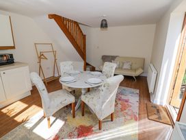A dining area with a round table set with plates and glasses surrounded by four floral chairs near a wooden staircase and a beige sofa at Little Barn Dodwell near Stratford-Upon-Avon