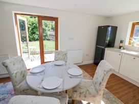 A dining area with a round table set for four and floral upholstered chairs near a kitchen with a black fridge and white cabinets at Little Barn in Dodwell near Stratford-Upon-Avon