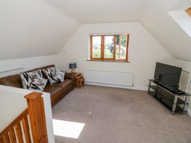 A living room with a brown leather sofa and patterned cushions a TV on a black stand and a wooden window at Little Barn in Dodwell near Stratford-Upon-Avon