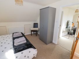 A bedroom with a bed, chair with a rolled blanket, wardrobe, and a visible adjacent room with a desk at Little Barn Dodwell near Stratford-Upon-Avon