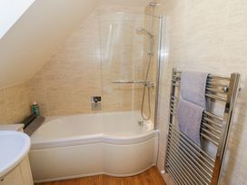 A bathroom with a bathtub shower combination, glass shower screen, towel radiator with towels, and beige tiled walls at Little Barn in Dodwell near Stratford-Upon-Avon