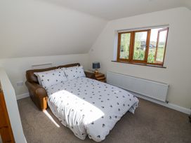A bedroom with a brown leather sofa bed with white patterned bedding a side table with a lamp and a window at Little Barn in Dodwell near Stratford-Upon-Avon