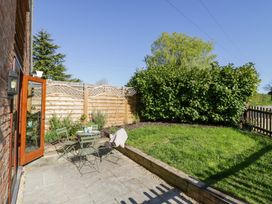 A garden with a small table and chairs on a paved patio next to a grassy area with bushes and a wooden fence at Little Barn in Dodwell near Stratford-Upon-Avon