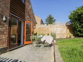 A patio with a small table and chairs outside a brick house with wooden doors at Little Barn in Dodwell near Stratford-Upon-Avon