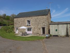 A stone building with a patio table and chairs under an umbrella and an adjacent wooden shed at Puddaven Barn in North Bovey near Chagford