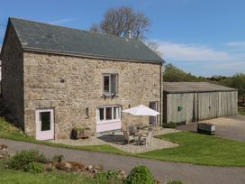 A stone barn with outdoor table and chairs under an umbrella next to a wooden shed at Puddaven Barn in North Bovey near Chagford