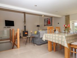 A living and dining area with a dining table set for four a sofa stove and wall mounted tv at Puddaven Barn in North Bovey near Chagford