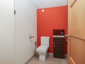A bathroom with a white toilet and wooden cabinet with sink against a red wall at Puddaven Barn in North Bovey near Chagford