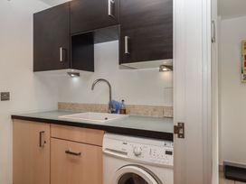 A laundry area with dark wall cabinets a sink and a washing machine at Puddaven Barn North Bovey near Chagford